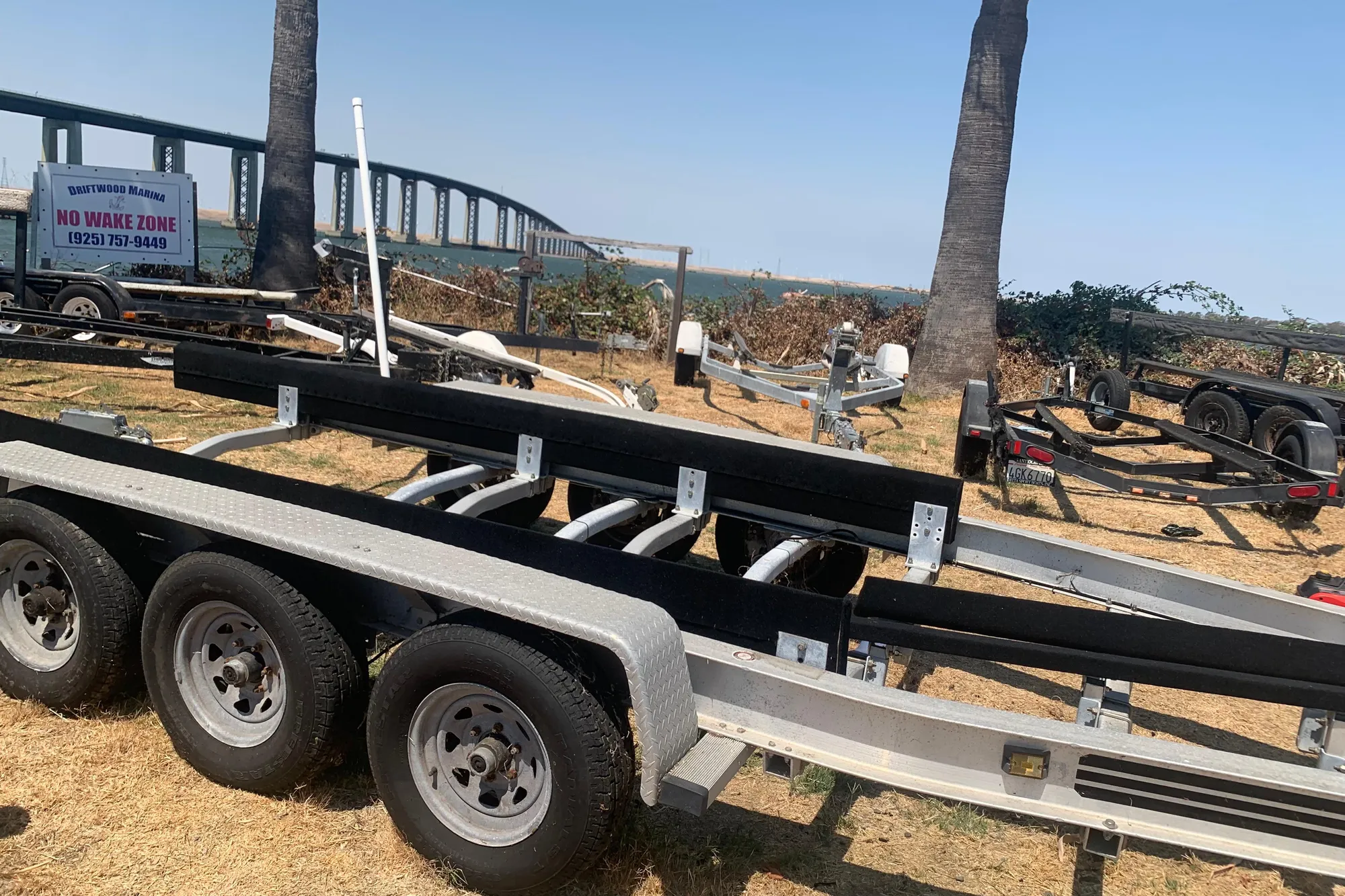 Boat trailer near Driftwood Marina, with bridge and "No Wake Zone" sign in background.