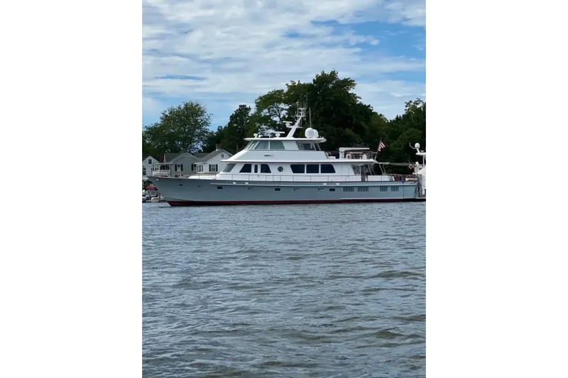 Sea Bold Yacht Photos Pics 2003 New England Boatworks Enclosed Raised Pilothouse yacht on calm water, with trees and houses in background.