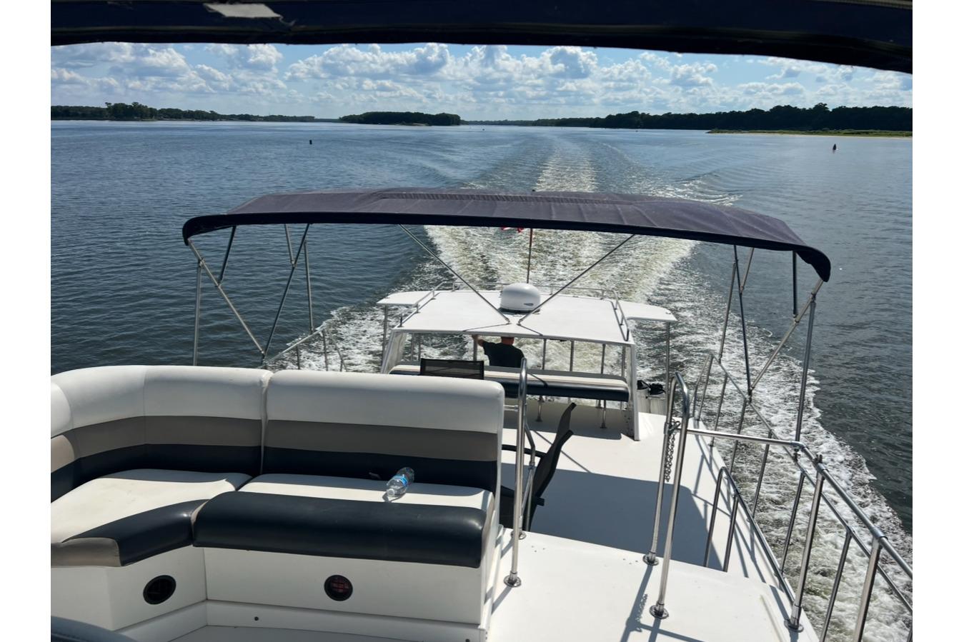 2002 Harbor Master 440 Widebody cruising on a sunny day with canopy and seating area.
