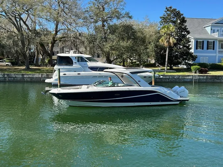  Yacht Photos Pics 2023 Sea Ray SLX 310 OB boat on a calm waterway, surrounded by trees and houses.