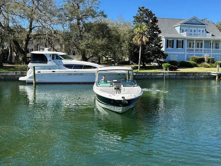  Yacht Photos Pics 2023 Sea Ray SLX 310 OB boat cruising on a serene waterway near a waterfront home.