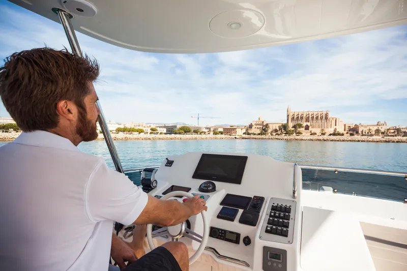 Salacia Yacht Photos Pics Man steering 2019 Sirena 64 yacht with scenic coastal view.