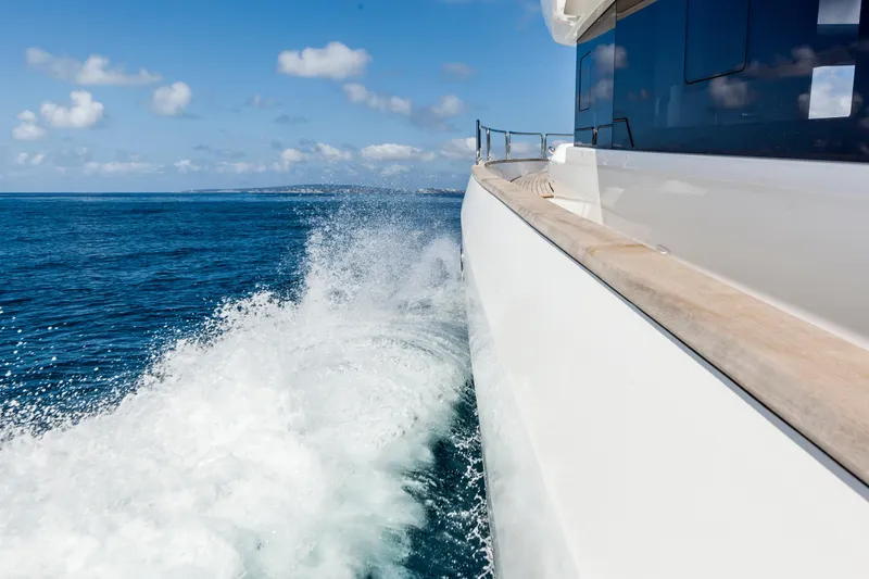 Salacia Yacht Photos Pics Sirena 64 yacht cruising on open sea, creating waves, under a clear blue sky.