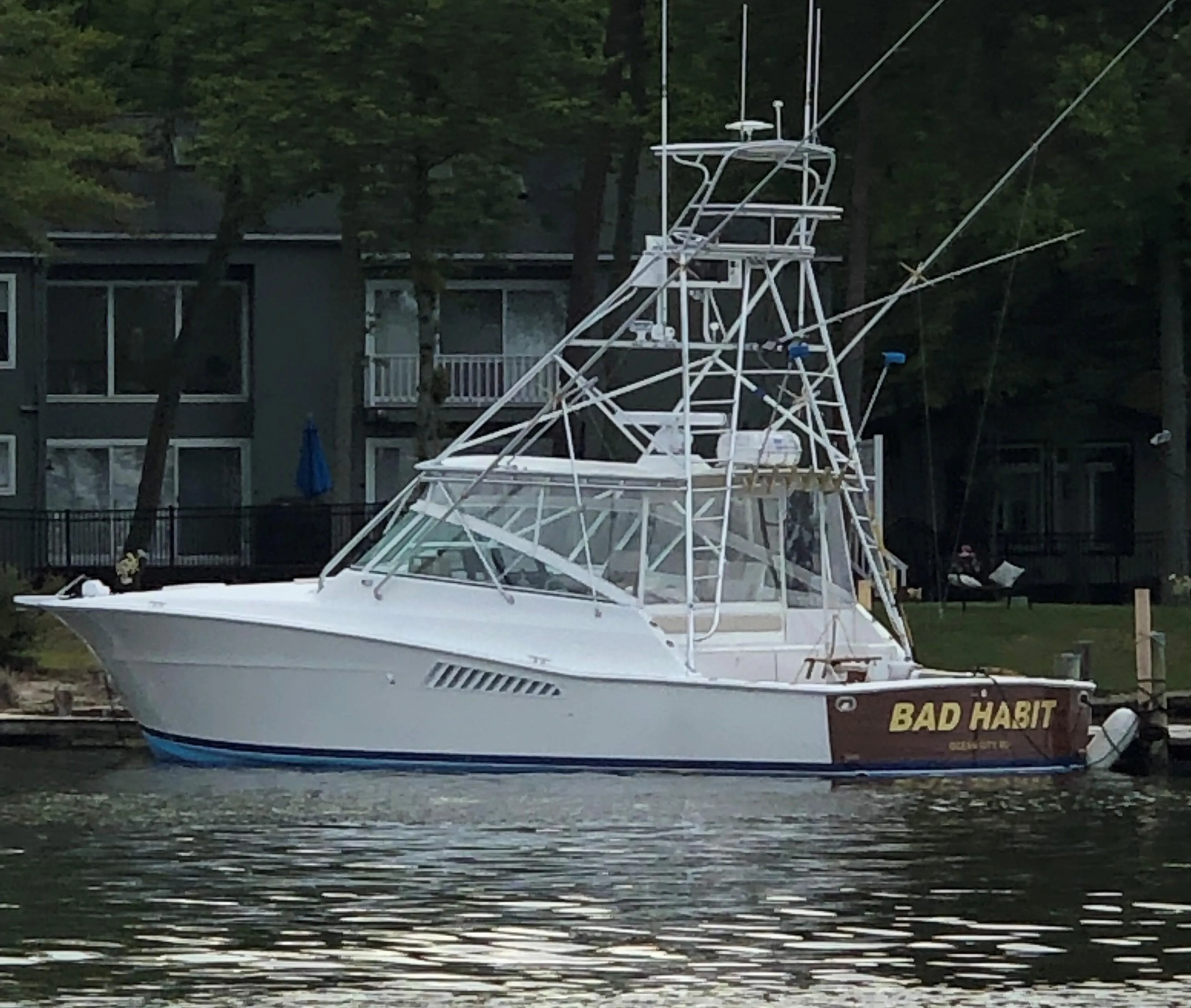 1997 Viking 43 Open yacht named "Bad Habit" docked by lakeside homes.