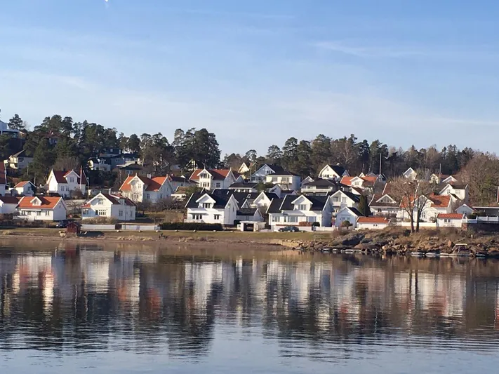  Yacht Photos Pics Scenic waterfront village with charming houses reflecting on calm water under a clear blue sky.