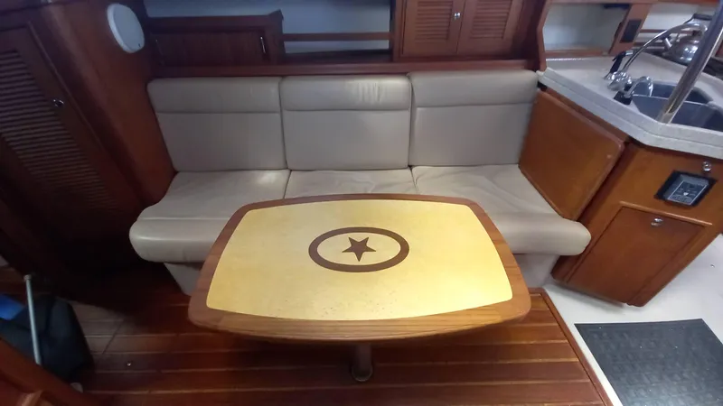 Sunny Girl Yacht Photos Pics Interior of 2004 Island Packet 370 sailboat with cushioned seating and star-embellished wooden table.