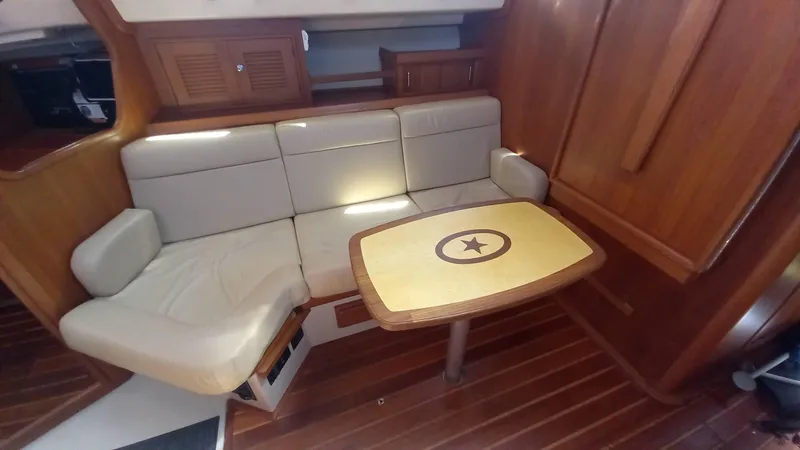 Sunny Girl Yacht Photos Pics Interior of 2004 Island Packet 370 sailboat with cushioned seating and wooden table.