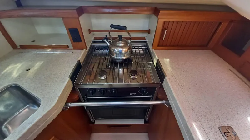 Sunny Girl Yacht Photos Pics 2004 Island Packet 370 yacht kitchen with stove, kettle, and wooden cabinetry.