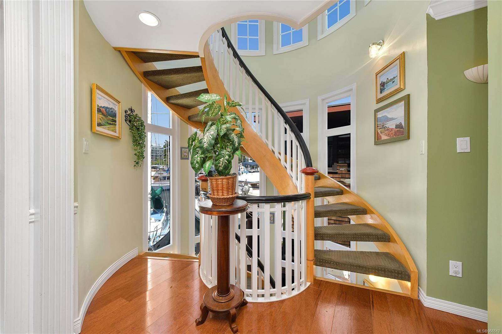 Elegant spiral staircase in a custom 2005 float home with wooden floors and decorative plants.