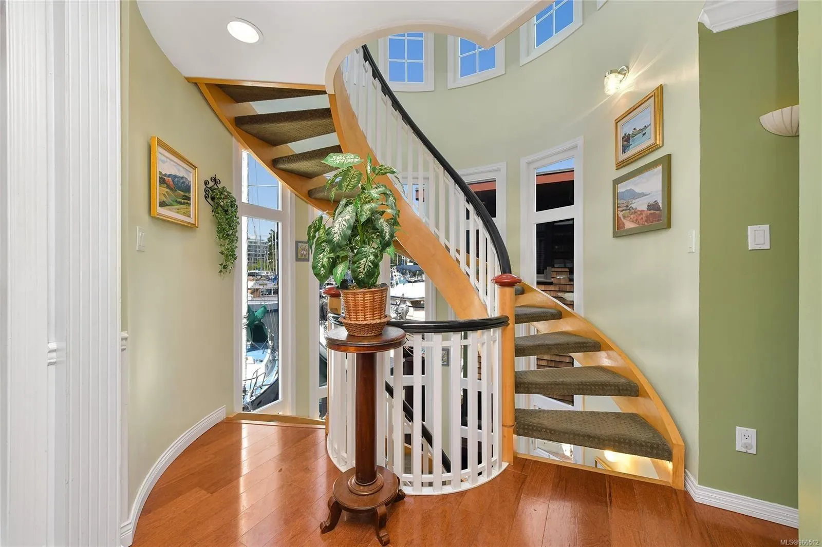 Elegant spiral staircase in a custom 2005 float home with wooden floors and decorative plants.