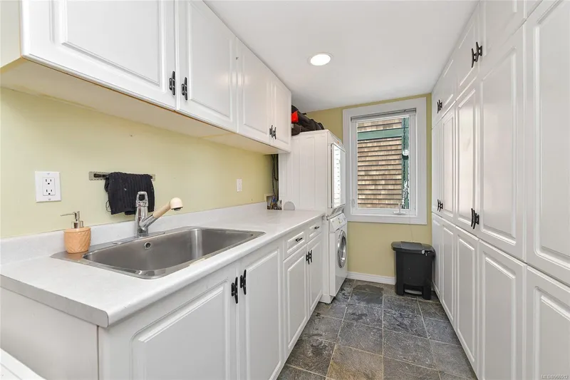  Yacht Photos Pics Laundry room with white cabinets, stainless steel sink, and slate flooring in a 2005 custom float home.