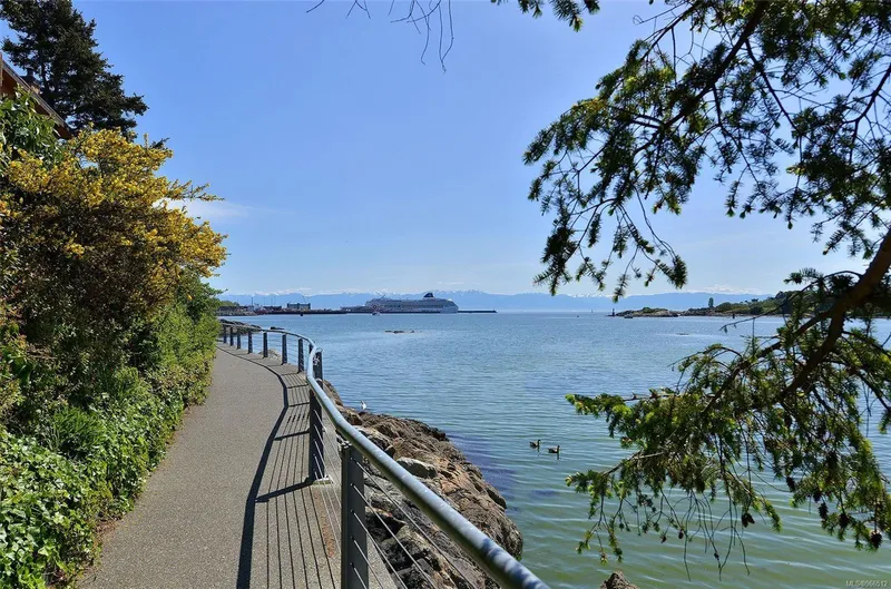  Yacht Photos Pics Scenic waterfront path with railing, overlooking calm sea and distant ferry under clear blue sky.