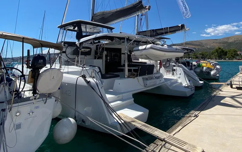  Yacht Photos Pics 2024 Lagoon 42 catamaran docked at marina, sunny day, clear blue sky.