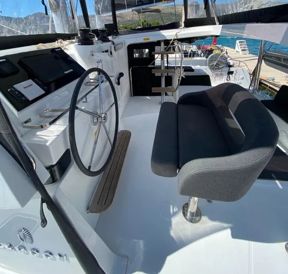  Yacht Photos Pics 2024 Lagoon 42 yacht cockpit with steering wheel and seating, docked by the sea.