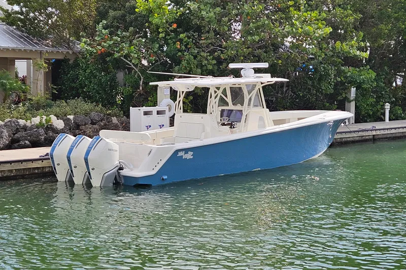 Seavee Yacht Photos Pics 2023 SeaVee 370z boat docked, featuring triple outboard engines, in a lush, green marina setting.
