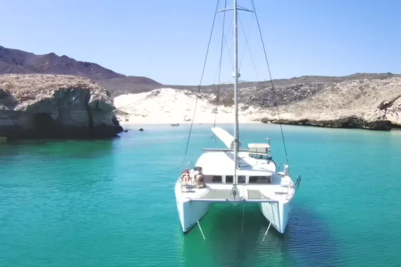 Arias Song Yacht Photos Pics 2016 Lagoon 400 S2 catamaran in a serene turquoise bay with rocky cliffs.