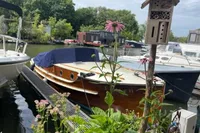 1926 custom motorboat docked, surrounded by flowers and greenery, with a birdhouse nearby.