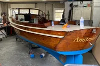 Vintage 1926 custom motorboat in workshop, wooden hull, named "Amsterdam," undergoing maintenance.
