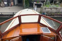 1926 custom motorboat with wooden deck and solar panel, docked near a garden.