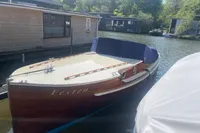 Vintage 1926 custom motorboat docked by houseboats on a sunny day.