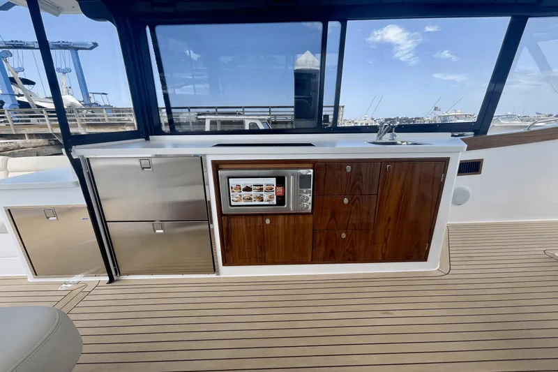  Yacht Photos Pics 2024 MJM 4 yacht interior with kitchenette, featuring wood cabinetry and stainless steel appliances.