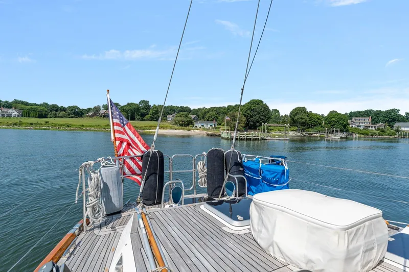 Mandate Yacht Photos Pics Deck view of 1996 Tayana 58 sailboat with American flag, near scenic shoreline.