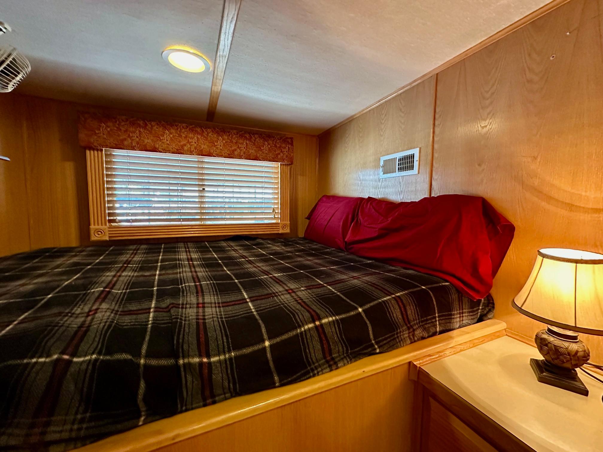 Cozy bedroom in 2004 Lakeview 16x68 houseboat with plaid bedding and warm lighting.