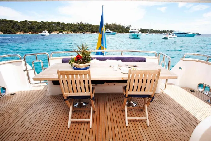  Yacht Photos Pics Luxury yacht deck with wooden table and chairs, overlooking serene blue waters.