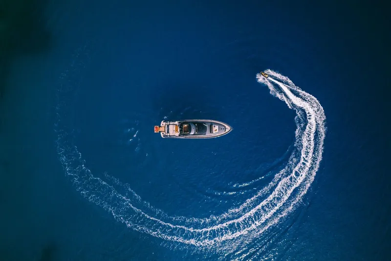 Who Cares Yacht Photos Pics Aerial view of 2006 Riva 68 Ego yacht with jet ski creating wake in blue ocean.