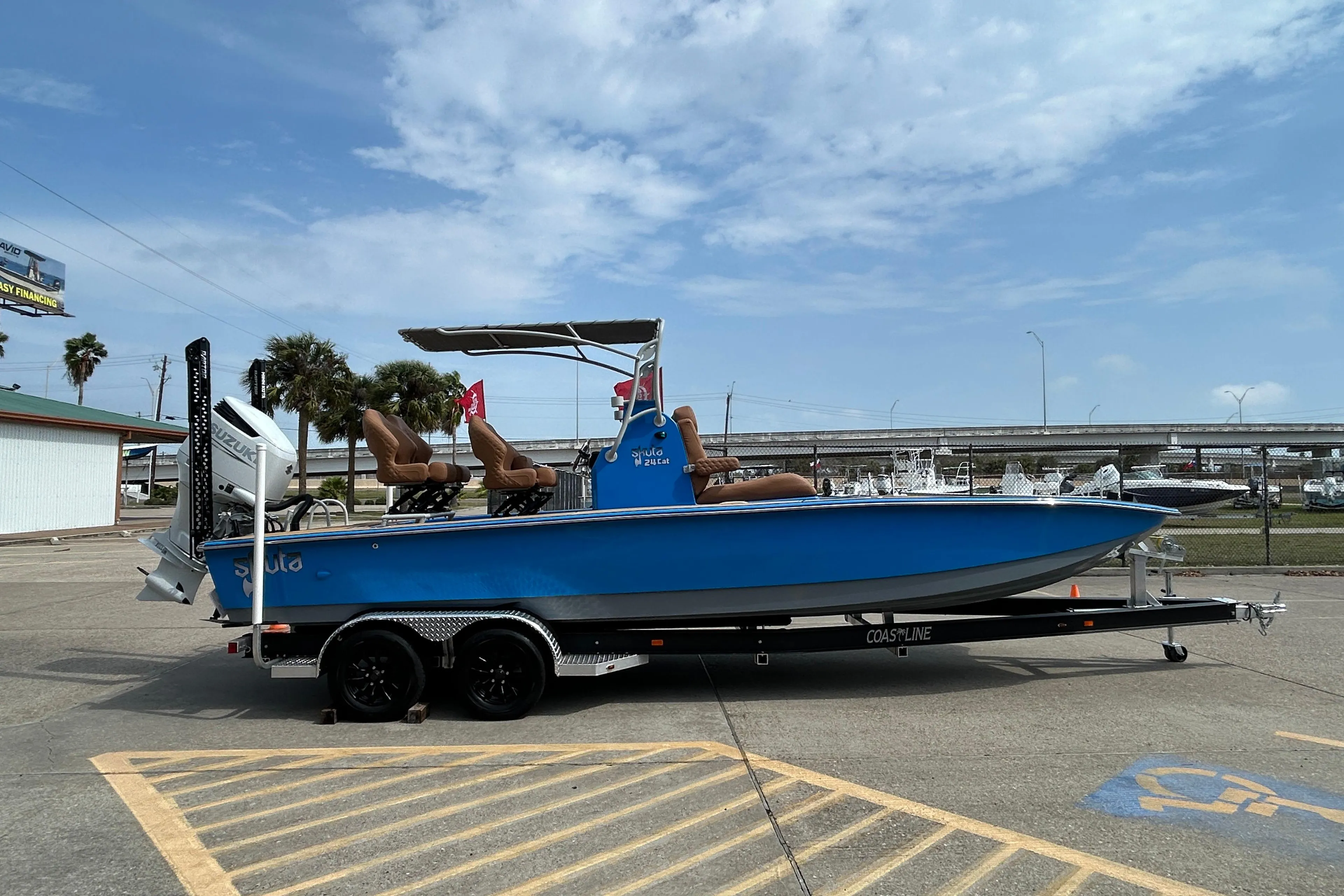 Blue 2026 Skuta 24 Skuta Cat boat on trailer, parked outdoors under a cloudy sky.