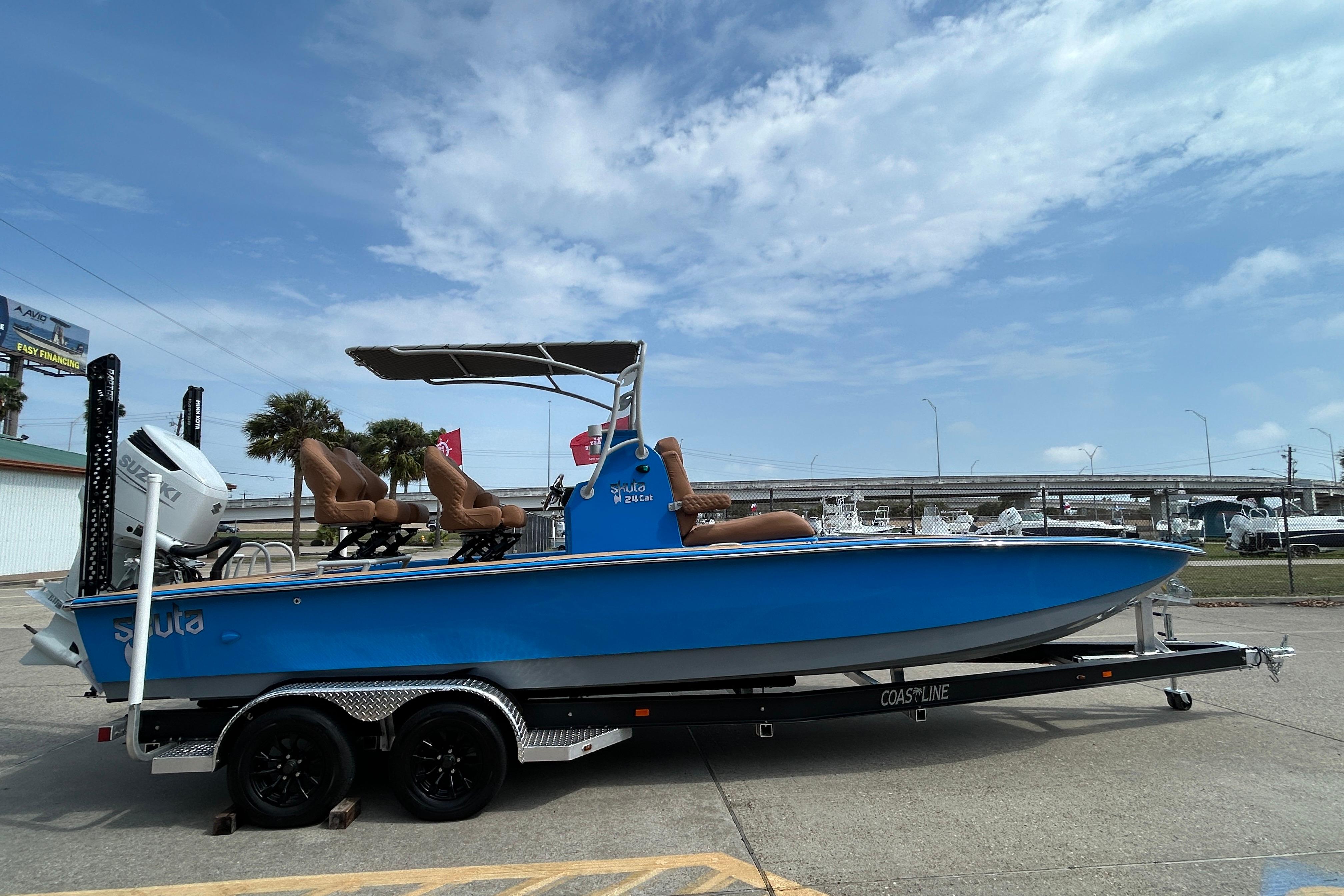 2026 Skuta 24 Skuta Cat boat on trailer, blue hull, outdoor setting.