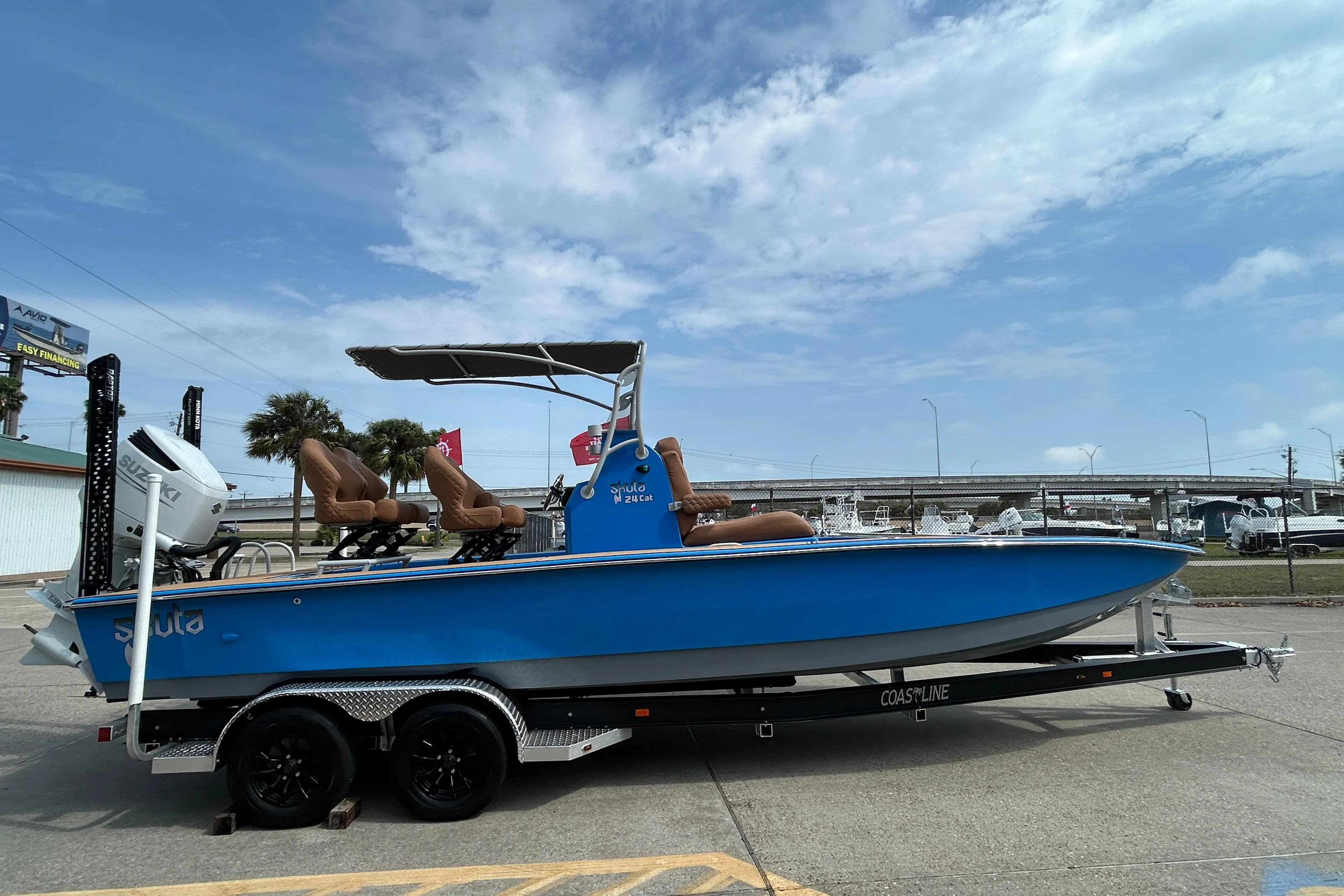 2026 Skuta 24 Skuta Cat boat on trailer, blue hull, outdoor setting.