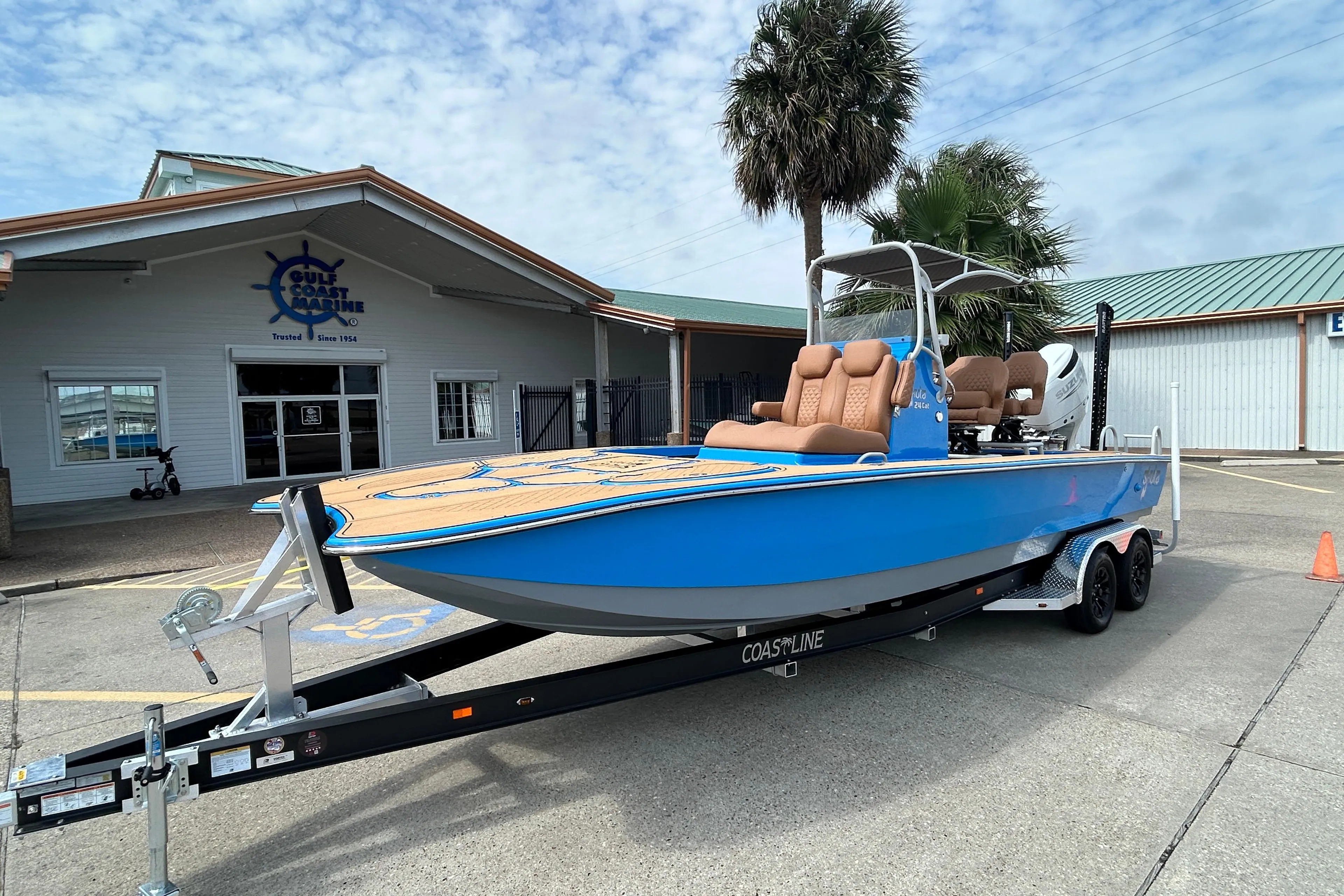 2026 Skuta 24 Skuta Cat boat on trailer outside Gulf Coast Marine building.