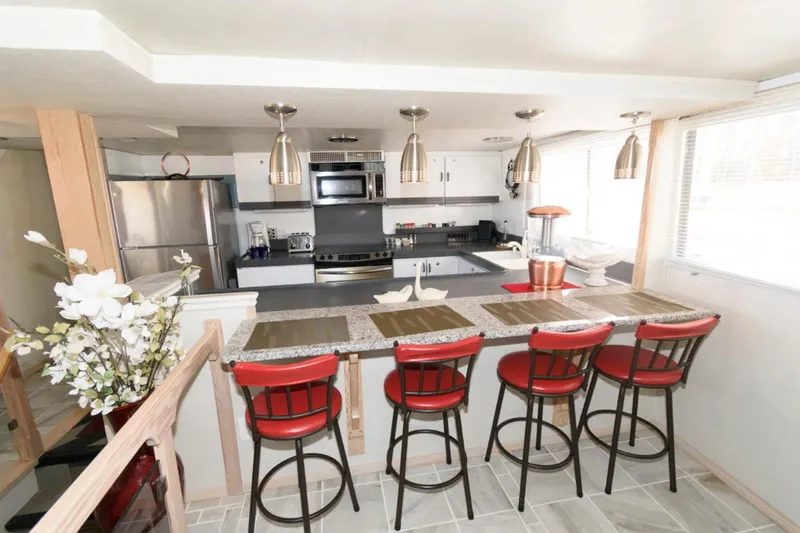 Liquidity Yacht Photos Pics Modern kitchen interior on 1984 Broward Raised Pilothouse yacht with red bar stools and stainless appliances.