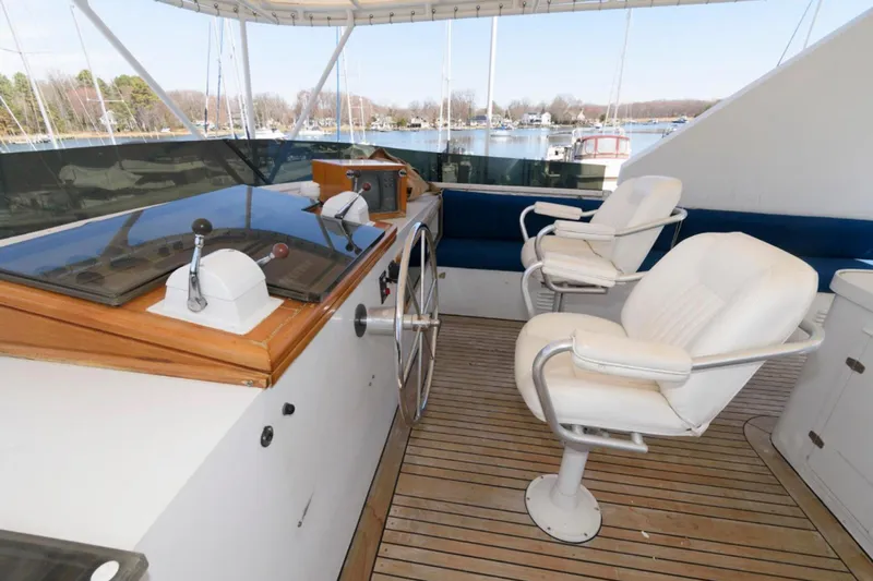 Liquidity Yacht Photos Pics 1984 Broward Raised Pilothouse yacht helm with white chairs and wooden deck.