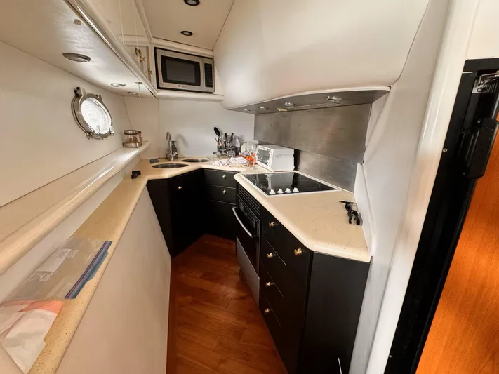 The Enterprise Yacht Photos Pics Compact kitchen in a 1995 Sunseeker MANHATTAN yacht with modern appliances and wood flooring.