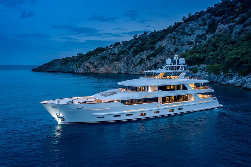 Sunrise Yacht Photos Pics Luxurious 2019 Yildiz 141 yacht illuminated at dusk near a rocky coastline.