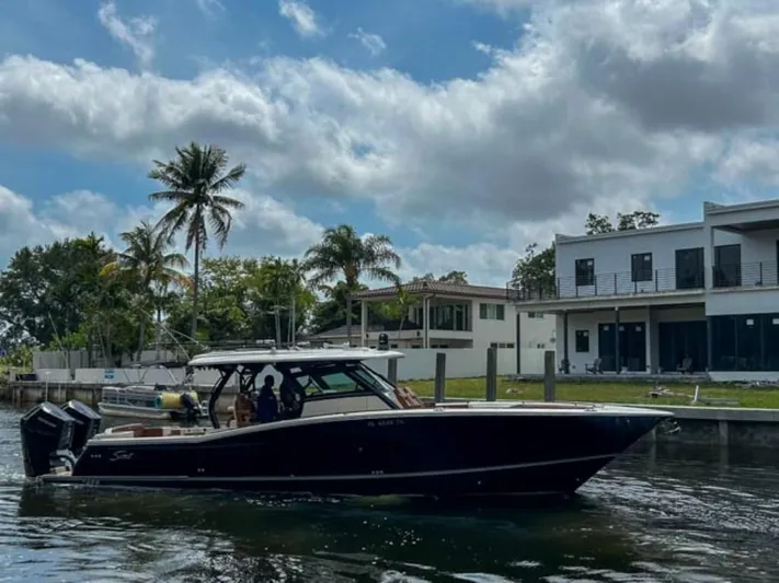  Yacht Photos Pics 2023 Scout 400 LXF boat cruising near waterfront homes with palm trees.
