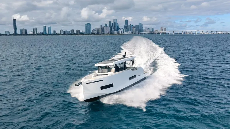  Yacht Photos Pics 2025 De Antonio Yachts D50 Coupé cruising near a city skyline on a sunny day.