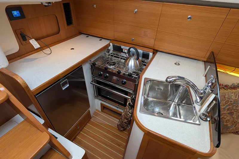 Uno Mas Yacht Photos Pics Modern galley kitchen in 2021 Catalina 315 sailboat with stove, sink, and wood cabinetry.