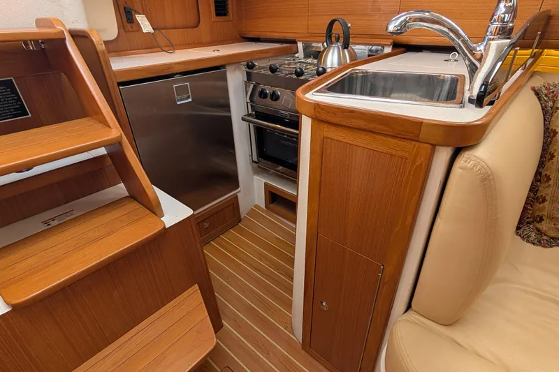 Uno Mas Yacht Photos Pics 2021 Catalina 315 yacht interior kitchen with wooden cabinetry, stainless steel appliances, and compact design.