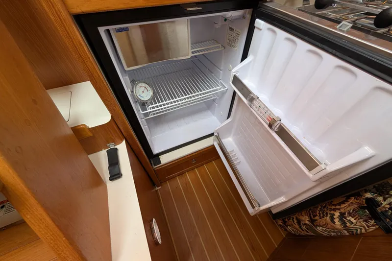 Uno Mas Yacht Photos Pics Open refrigerator inside 2021 Catalina 315 yacht, featuring wooden flooring and compact design.