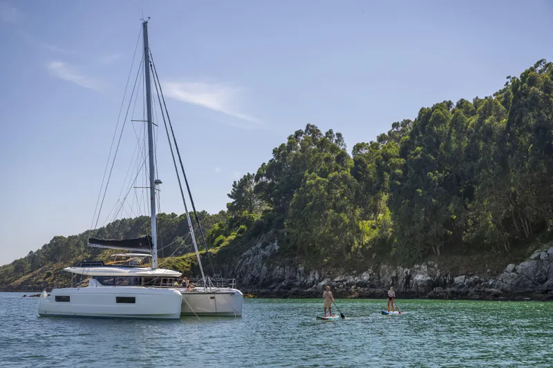  Yacht Photos Pics 2025 Lagoon 43 catamaran near paddleboarders in scenic coastal waters.