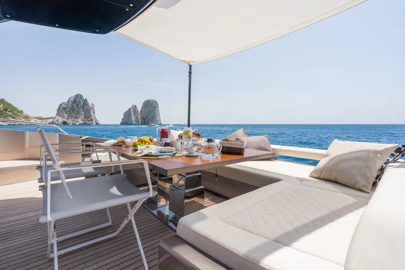 Kar Yacht Photos Pics Luxurious 2021 Riva 88 Folgore yacht deck with dining setup, ocean view, and coastal rocks.