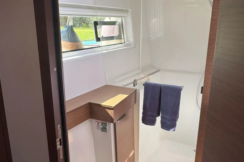 Keola Yacht Photos Pics 2022 Lagoon 40 yacht bathroom with window, wooden accents, and blue towels.