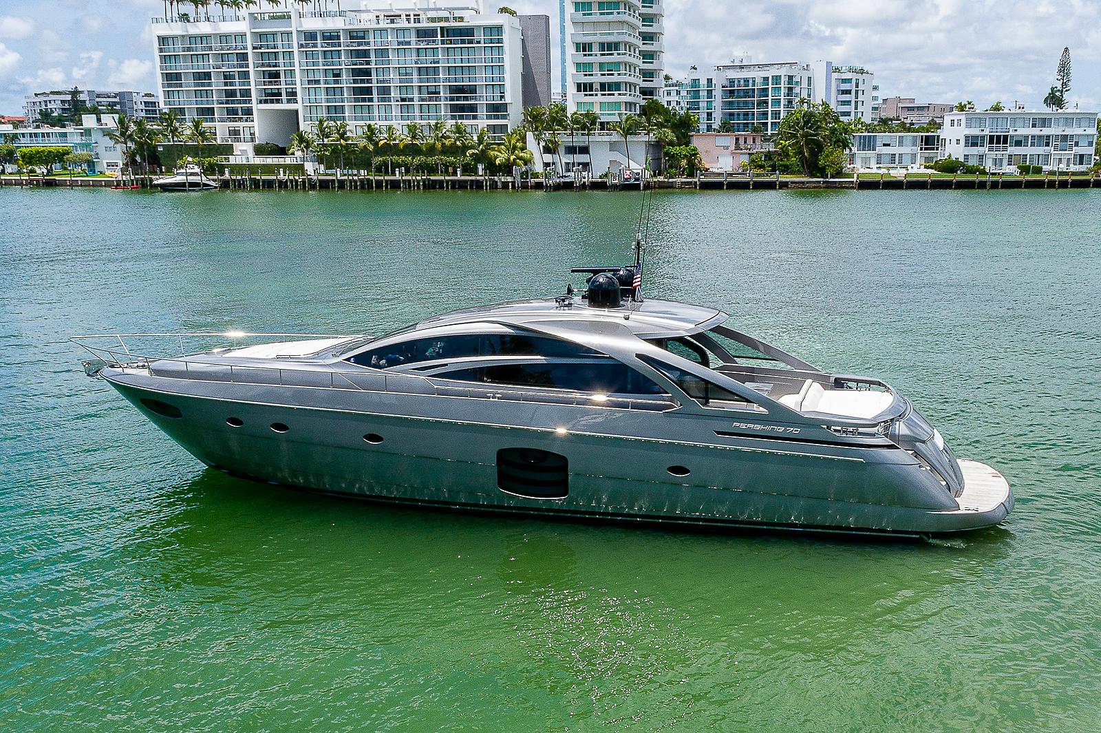 Luxury 2015 Pershing 70 yacht cruising on a serene waterway near modern buildings.