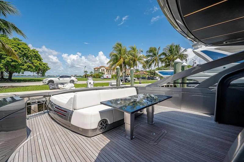 Andiamo Yacht Photos Pics Luxurious 2015 Pershing 70 yacht deck with seating and table, docked near palm trees.