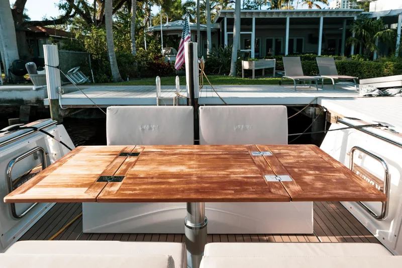 Next Yacht Photos Pics Fjord 38 Open 2022 boat with wooden table and seating area, docked near a modern house.