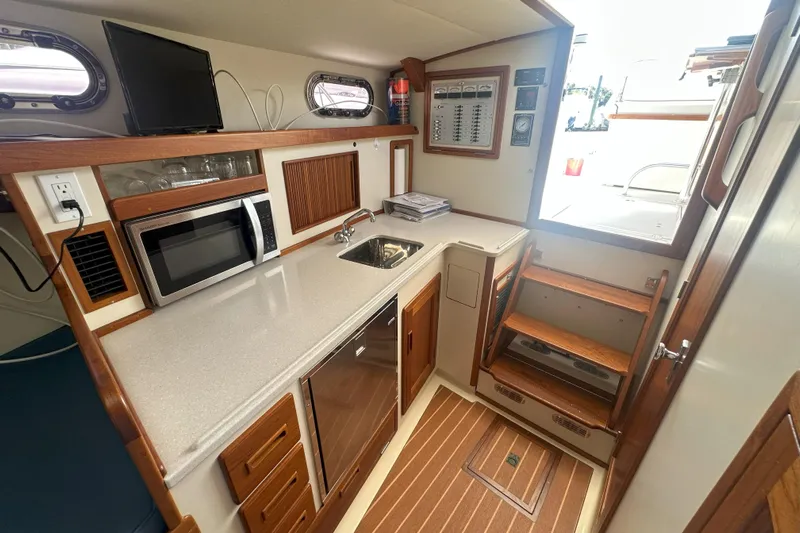 At Last 10 Yacht Photos Pics 2017 Fortier F-30 Hardtop boat interior with kitchenette, microwave, sink, and wooden cabinetry.