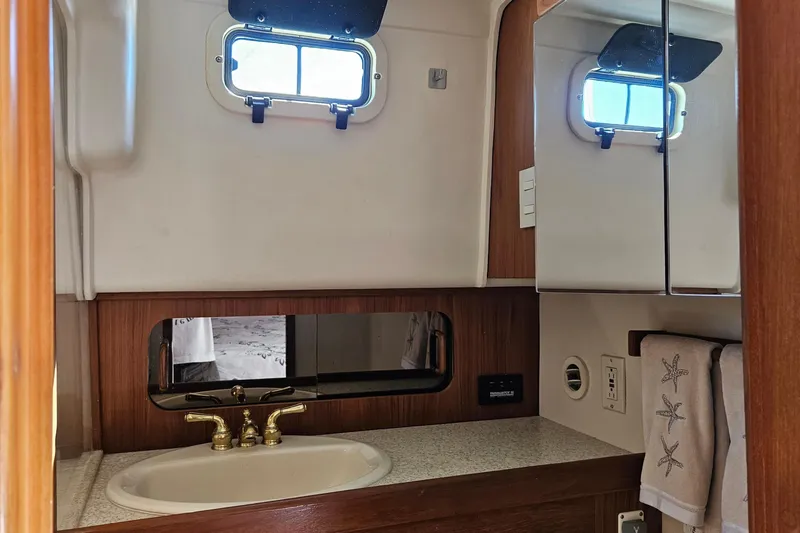  Yacht Photos Pics Bathroom interior of 1999 Mainship 430 Trawler with sink, mirror, and porthole window.